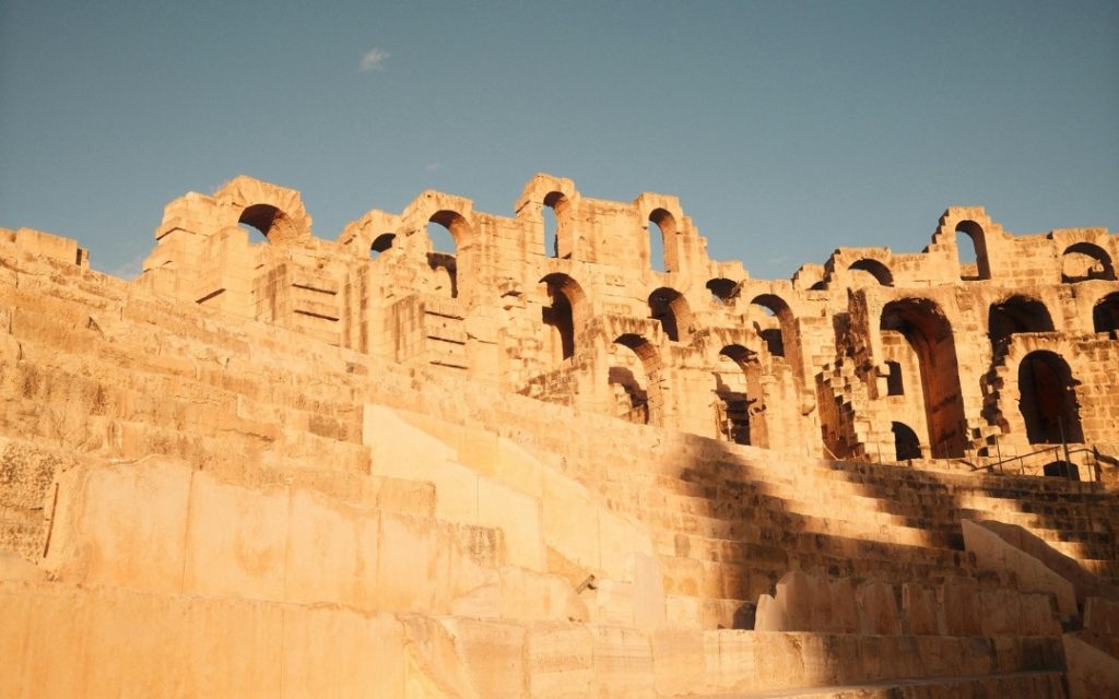 Zabytkowe arkady rzymskiego amfiteatru w Tunezji oświetlone ciepłym, popołudniowym słońcem.