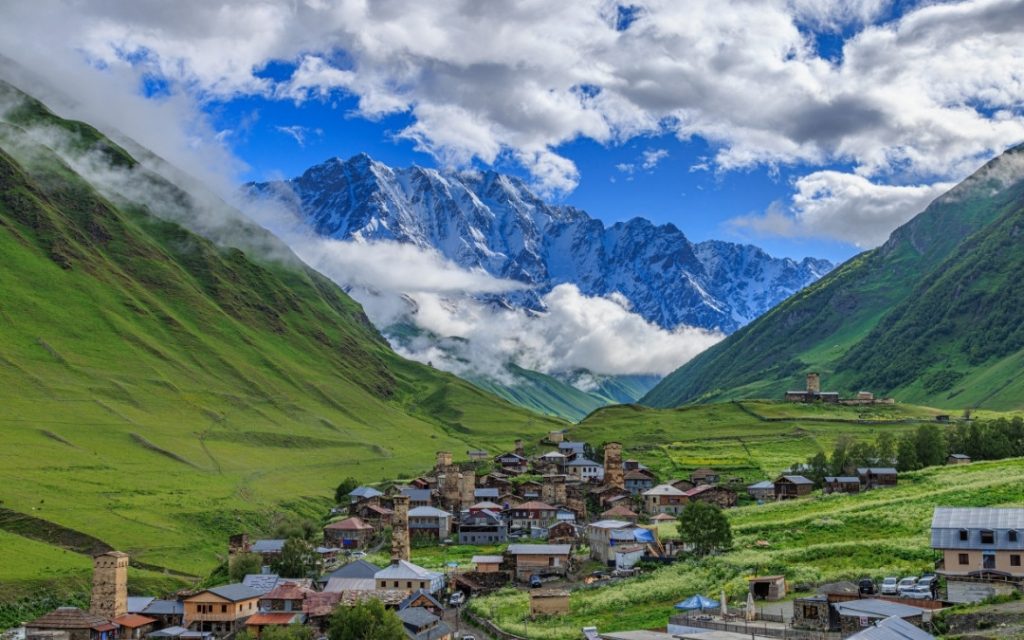Zielona górska dolina z małą wioską u stóp potężnych, ośnieżonych szczytów Kaukazu w Gruzji.