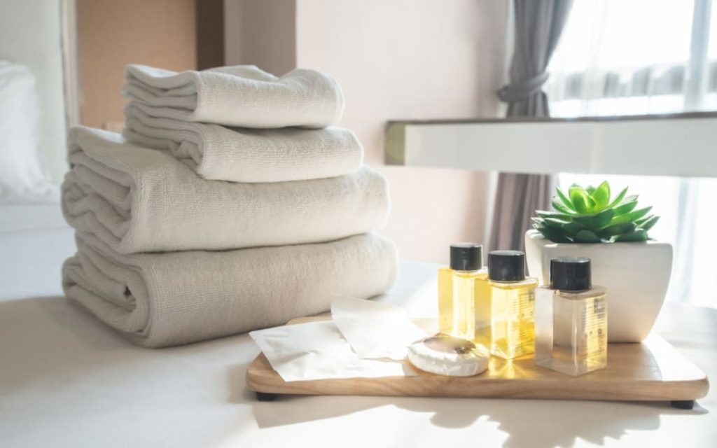 Białe ręczniki obok kosmetyków na łóżku hotelowym