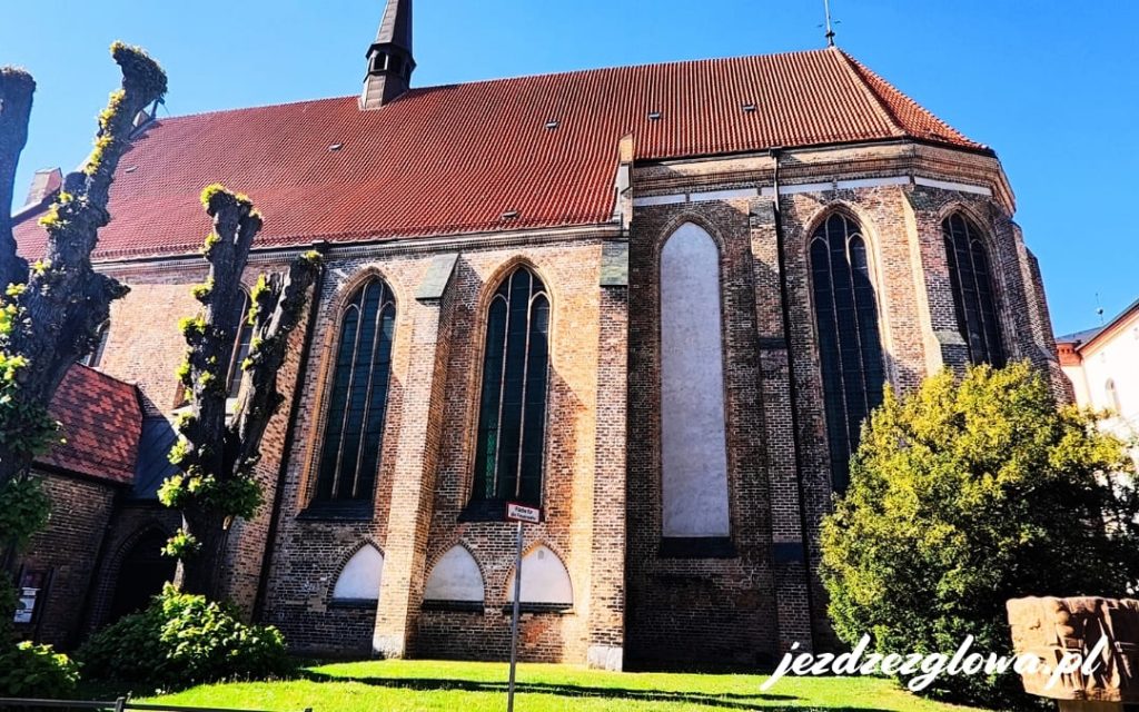 Klasztor Świętego Krzyża w Rostocku - piękny, zabytkowy kompleks gotycki z czerwonej cegły, otoczony roślinnością, z dawnym kościołem klasztornym dziś pełniący funkcję kościoła uniwersyteckiego