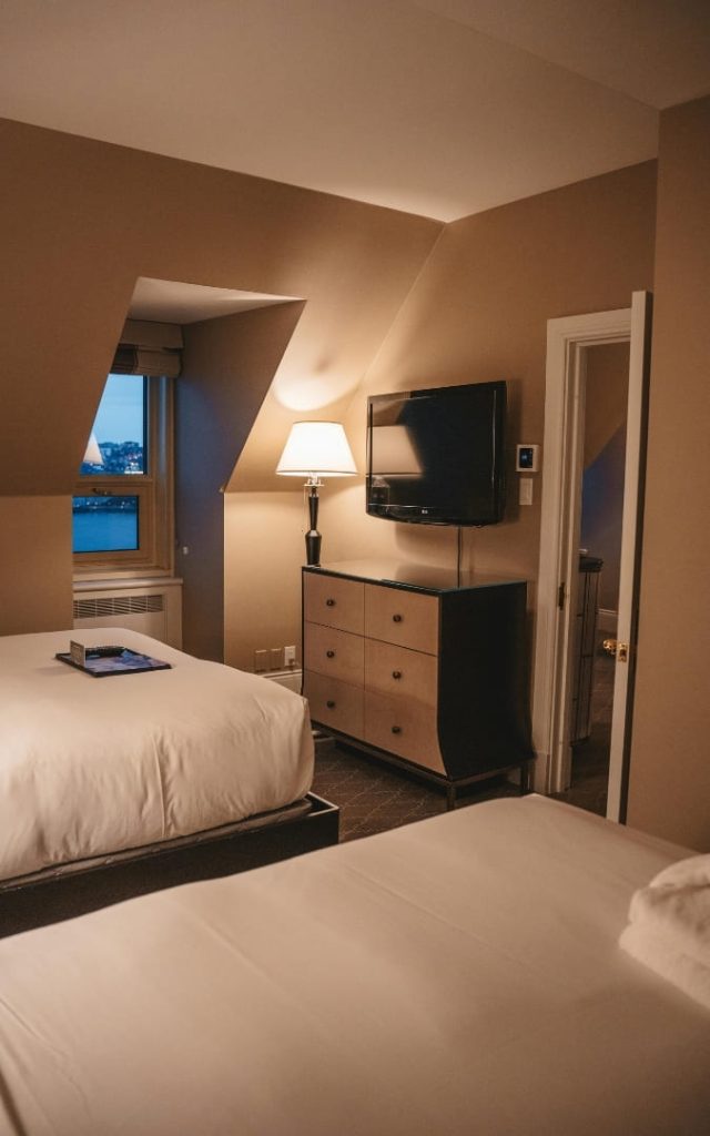 Przytulny pokój hotelowy z dwoma łóżkami, komodą i telewizorem w ciepłym świetle lampy