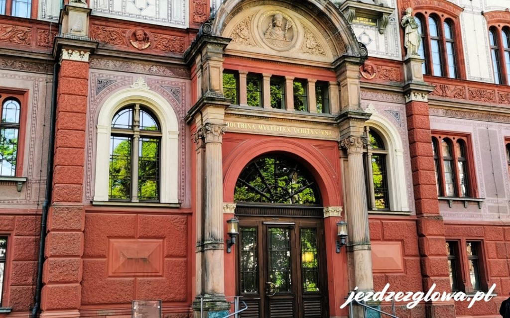Zbliżenie na wejście do gmachu Uniwersytetu w Rostocku, ceglaną fasadą i napisem ,,Nauk jest wiele, prawda jedna'' nad drzwiami