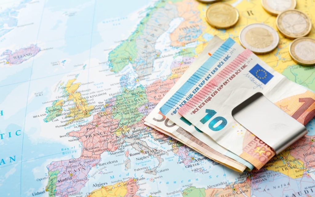 Banknoty i monety euro umieszczone na mapie Europy, symbolizujące koszty podróży, walutę oraz planowanie wyjazdu po krajach europejskich