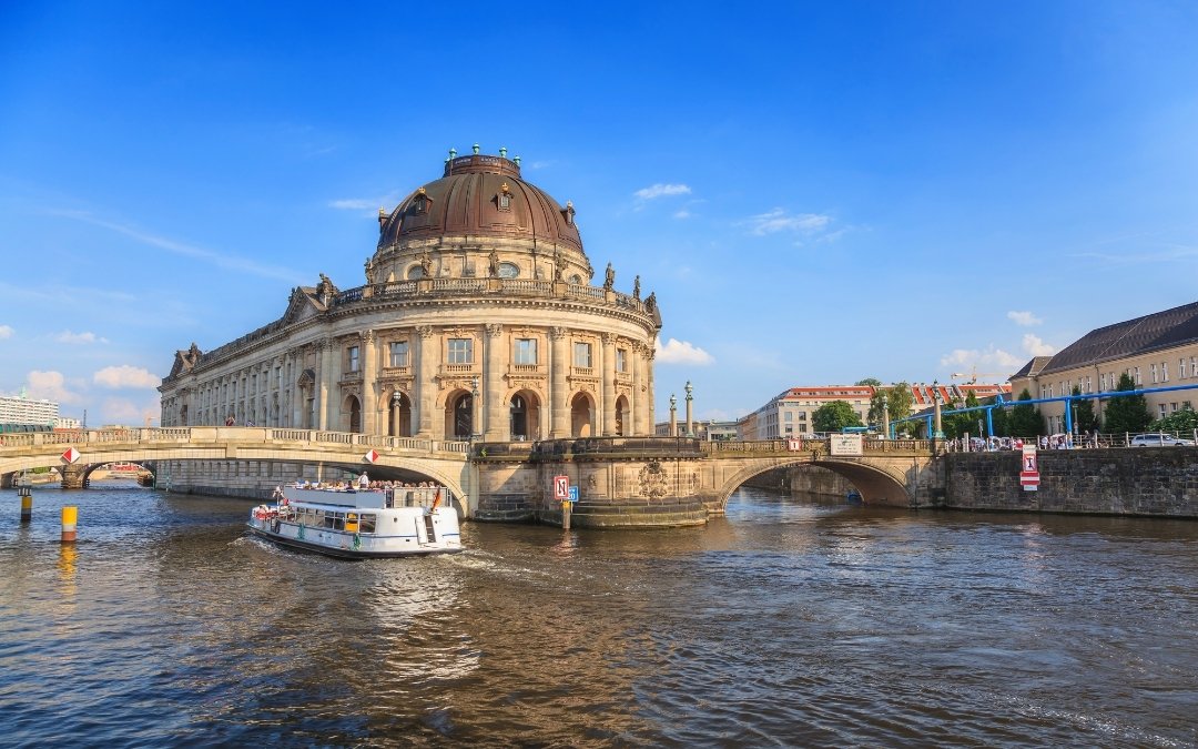 Bode-Museum na Wyspie Muzeów w Berlinie widziane od strony Sprewy, z łodzią wycieczkową płynącą przed zabytkową fasadą i kopułą muzeum