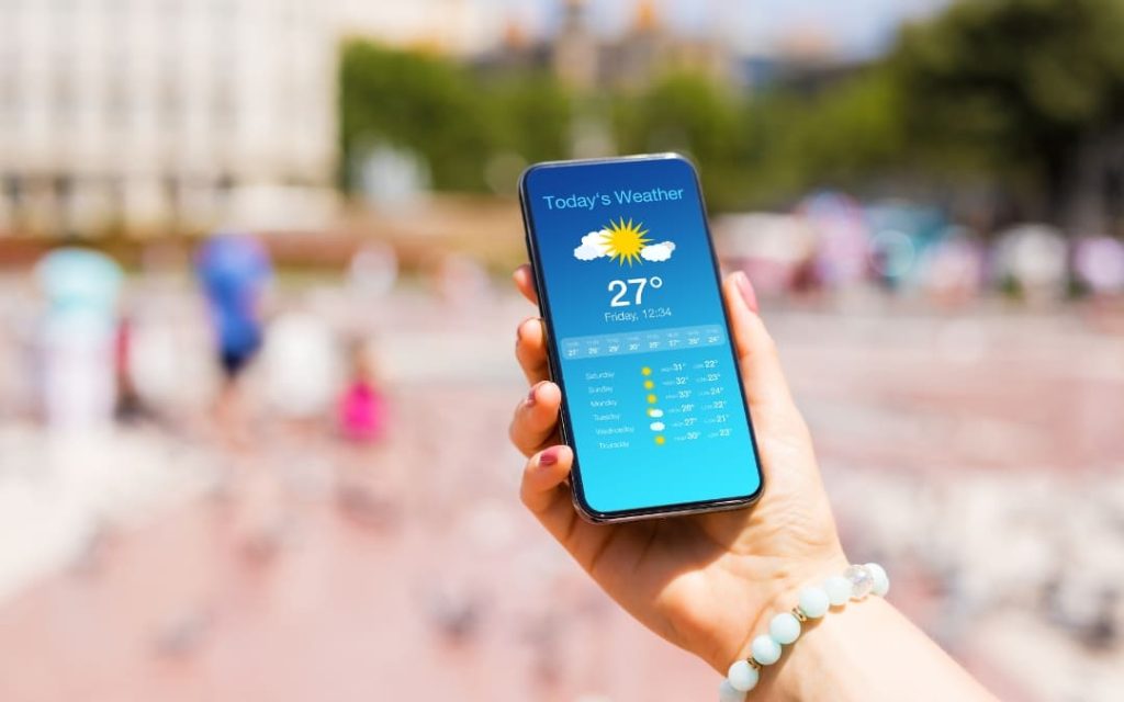 Dłoń trzymająca telefon z aplikacją pogodową pokazującą słoneczną pogodę 