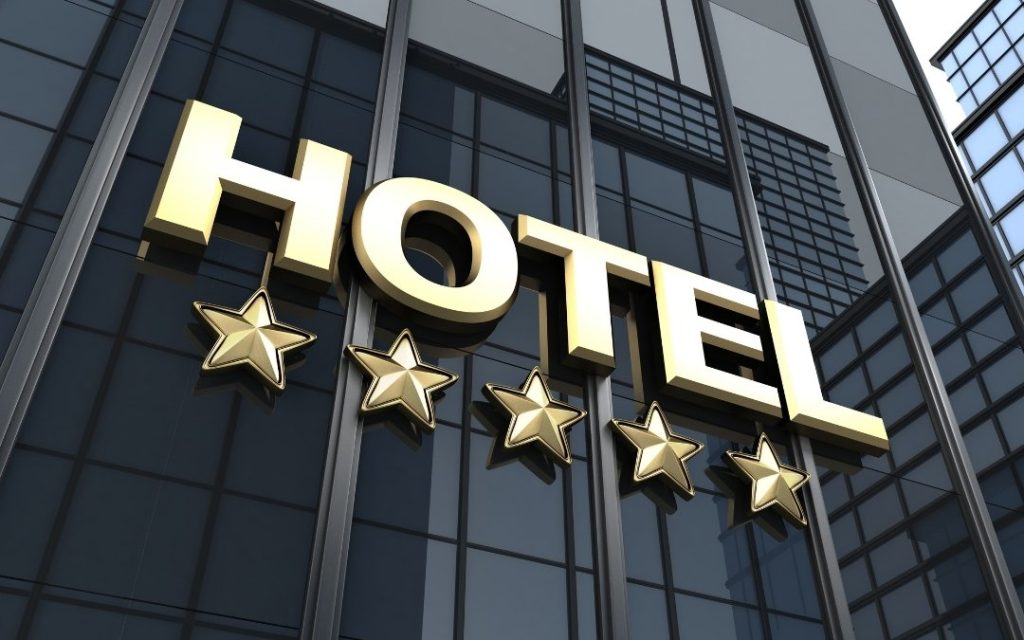 Duży napis Hotel z pięcioma złotymi gwiazdkami na nowoczesnej szklanej fasadzie budynku