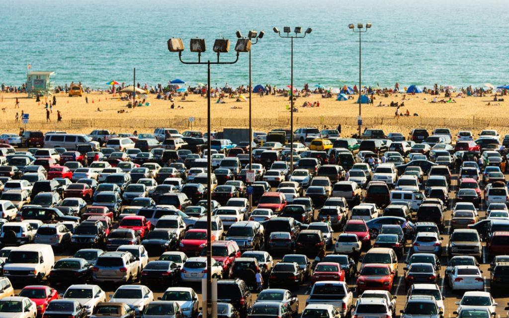Duży parking samochodowy przy plaży z widokiem na morze oraz licznymi pojazdami zaparkowanymi w rzędach