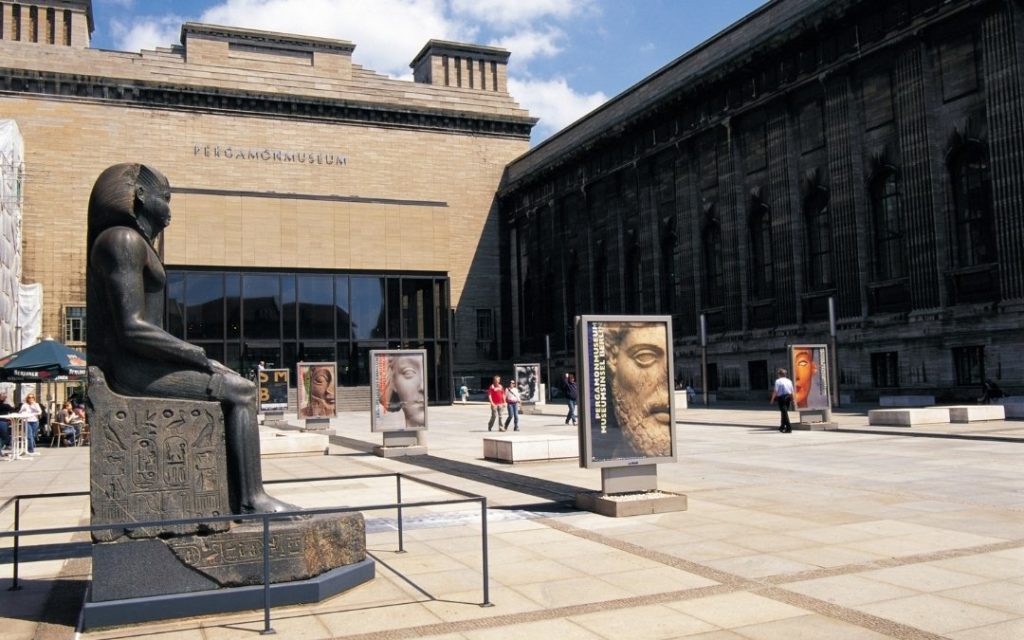 Dziedziniec przed Pergamonmuseum na Wyspie Muzeów w Berlinie, z dużą egipską rzeźbą i plakatami wystawienniczymi przy wejściu do muzeum
