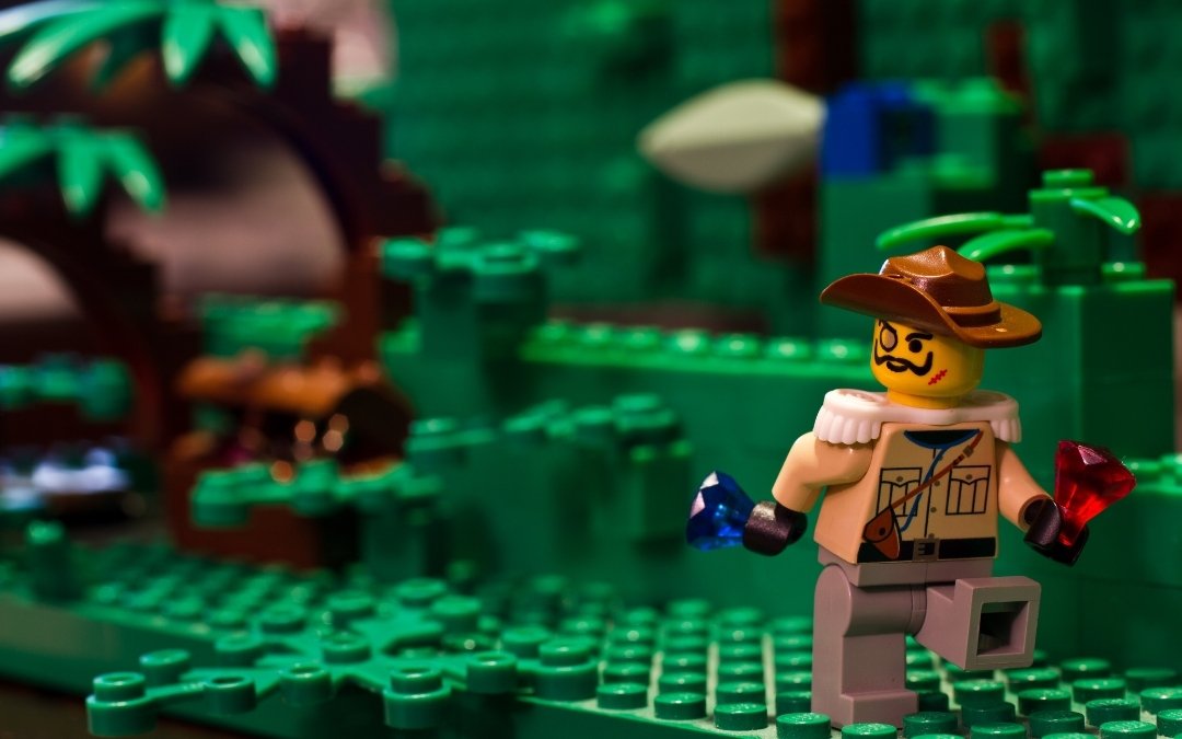Figurka LEGO poszukiwacza przygód w kapeluszu, trzymająca kolorowe klejnoty na zielonej makiecie dżungli z klocków