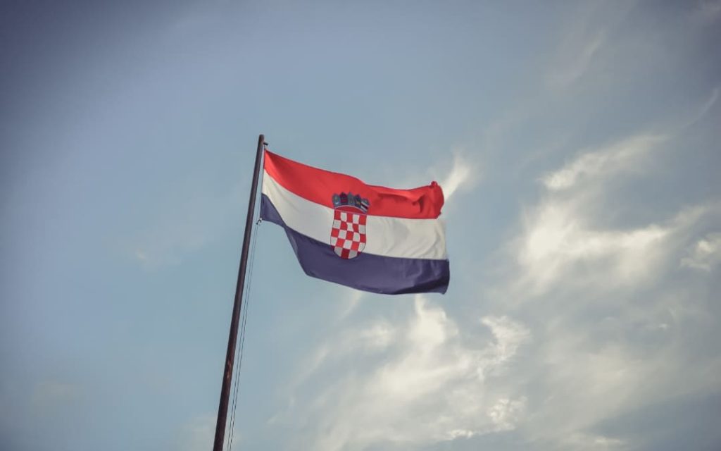 Flaga Chorwacji powiewająca na maszcie na tle jasnego nieba z rozproszonymi chmurami