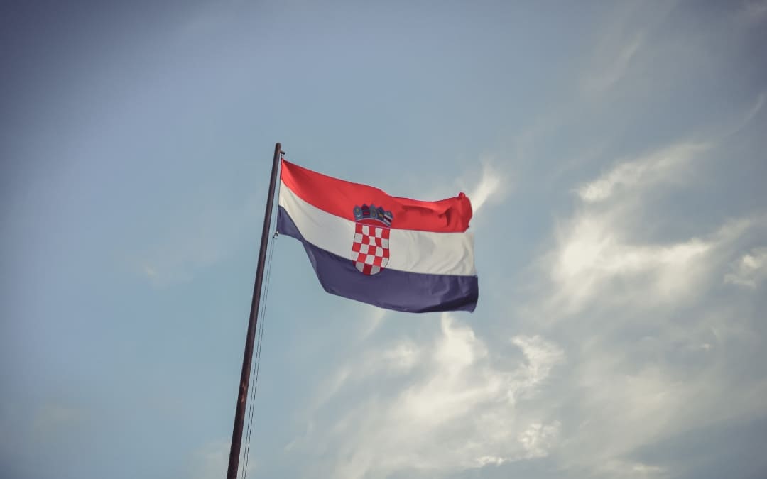 Flaga Chorwacji powiewająca na maszcie na tle jasnego nieba z rozproszonymi chmurami
