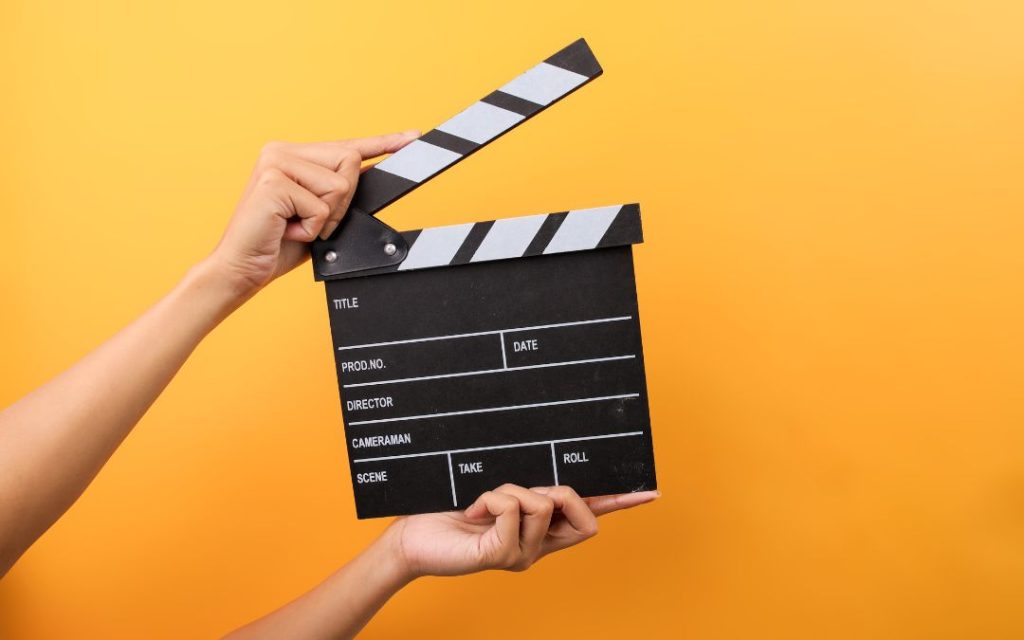 Klaps filmowy trzymany w dłoniach na żółtym tle
