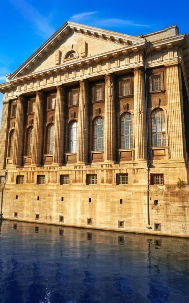 Klasycystyczna fasada Pergamonmuseum na Wyspie Muzeów w Berlinie, odbijająca się w wodzie kanału przy słonecznym świetle