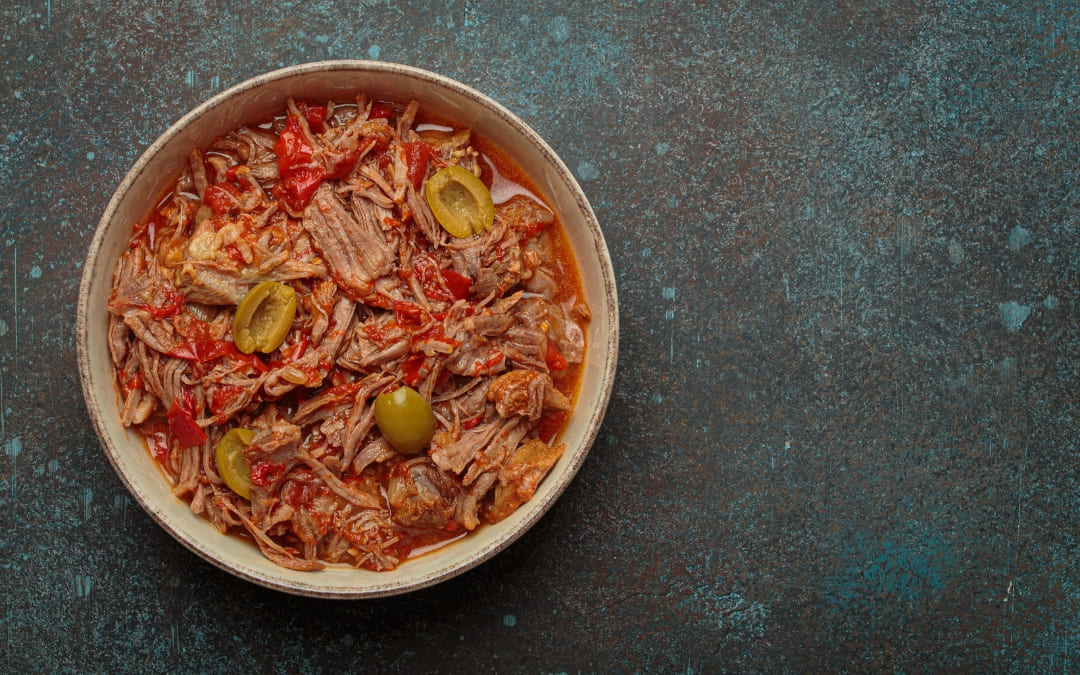 Miska ropa vieja z szarpanym mięsem, papryką, pomidorami i oliwkami na ciemnym tle