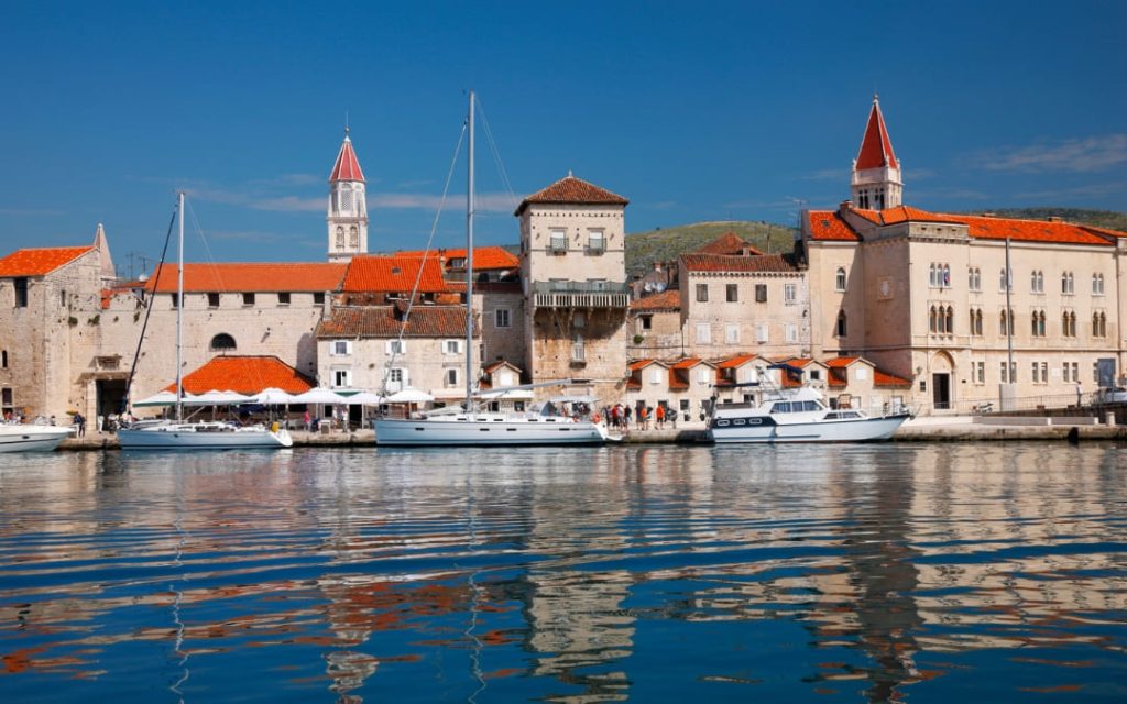 Nabrzeże starego miasta Trogir z jachtami, historyczną zabudową i wieżami katedry nad spokojną taflą morza