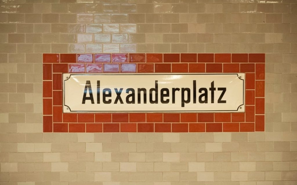 Napis Alexanderplatz na ścianie berlińskiej stacji, umieszczony na jasnych kafelkach z czerwoną ramką dekoracyjną