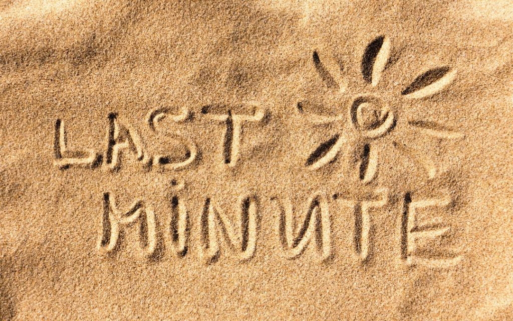 Napis Last Minute i rysunek słońca wykonane na jasnym piasku