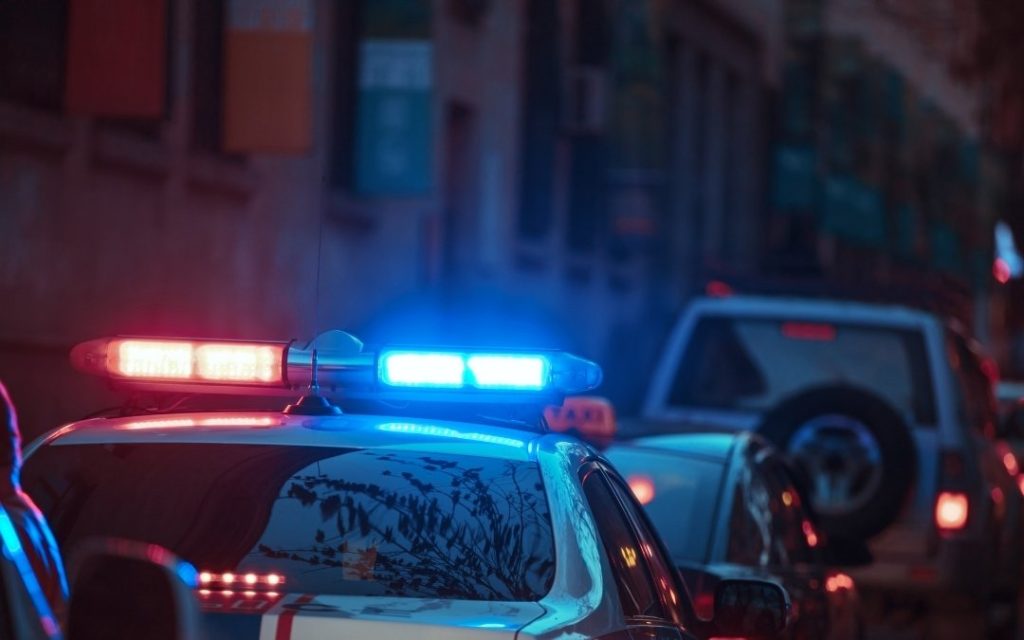 Nocne ujęcie samochodu służb ratunkowych z migającymi czerwono-niebieskimi światłami, stojącego na miejskiej ulicy wśród innych pojazdów