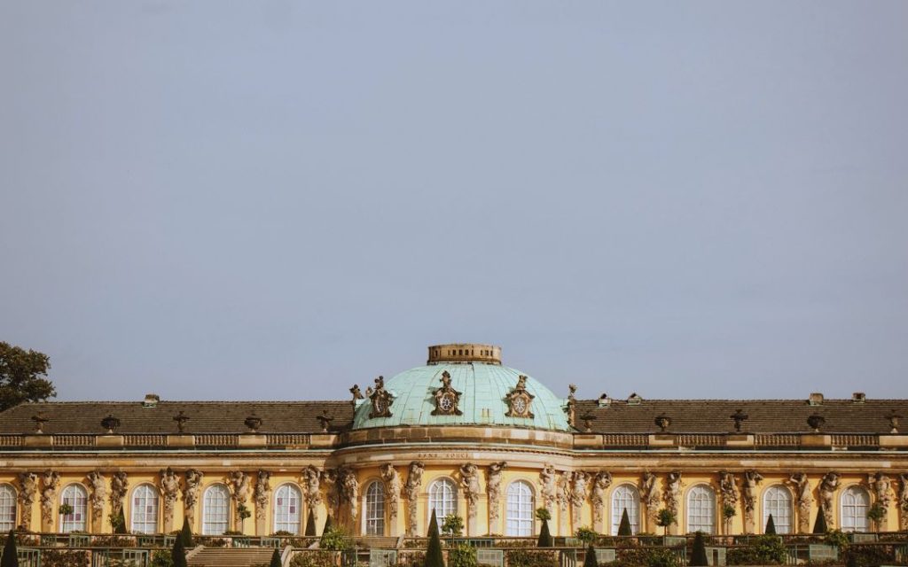 Pałac Sanssouci w Poczdamie z zieloną kopułą i żółtą fasadą na tle jasnego nieba