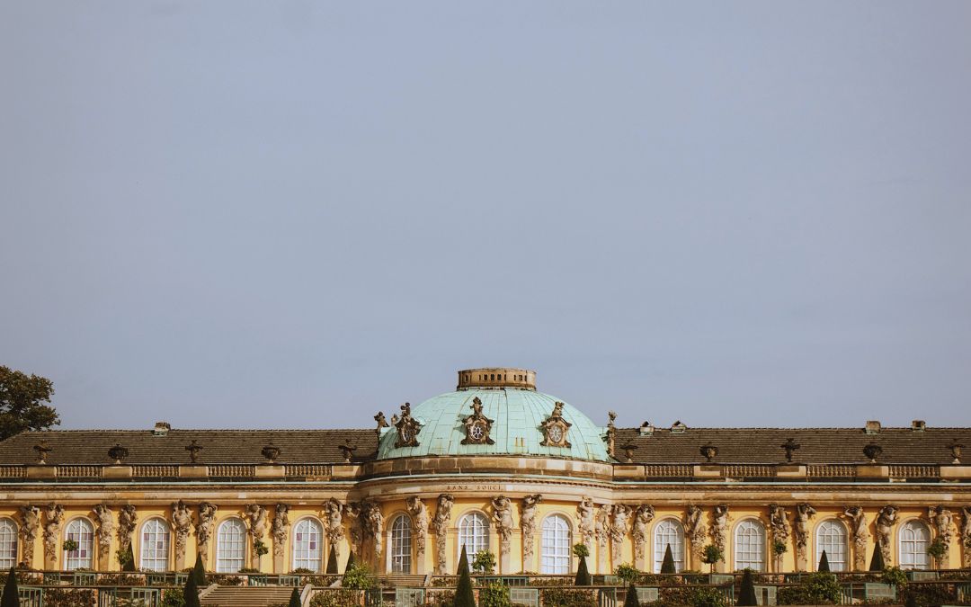 Pałac Sanssouci w Poczdamie z zieloną kopułą i żółtą fasadą na tle jasnego nieba
