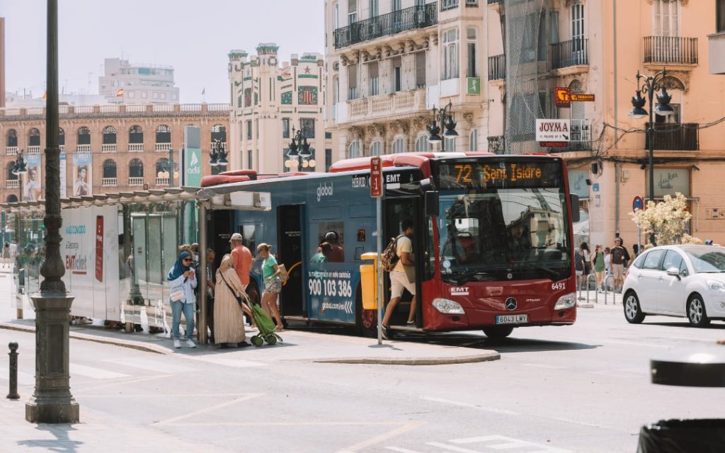 Pasażerowie wsiadający do autobusu miejskiego na przystanku przy ruchliwej ulicy