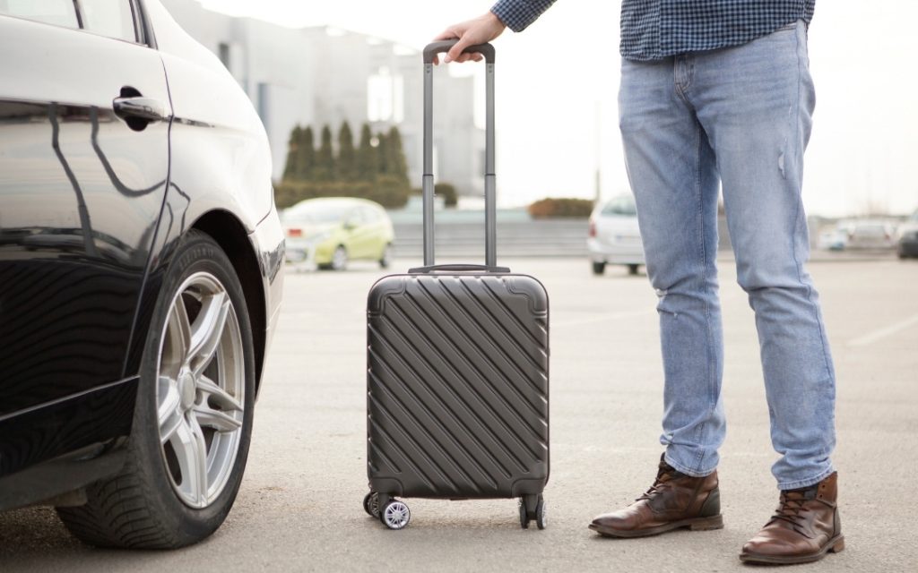 Podróżny z walizką stojący przy samochodzie na parkingu