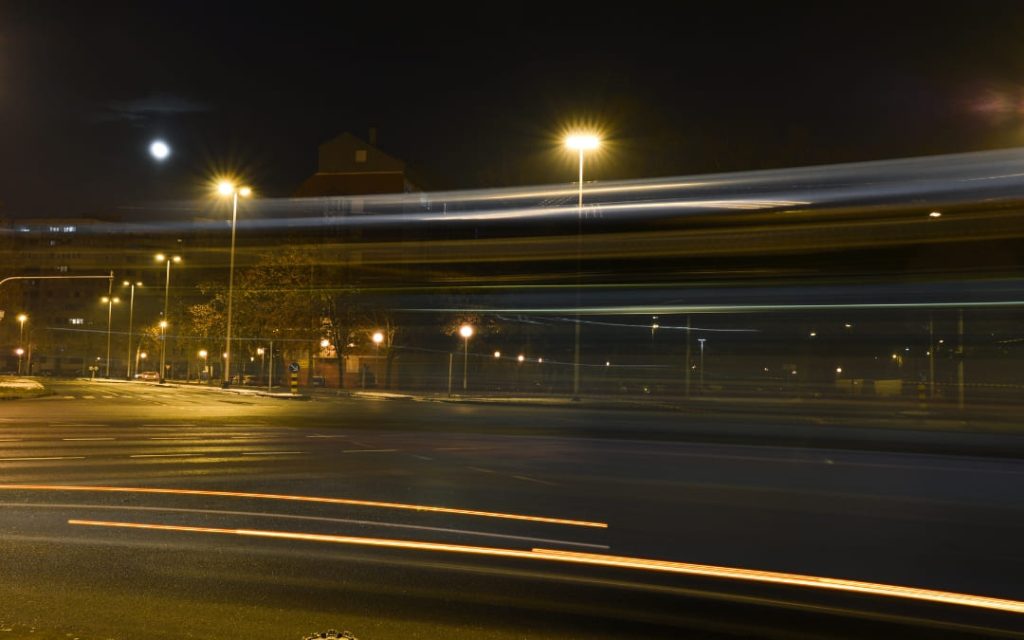 Rozmyty autobus miejski przejeżdżający nocą przez oświetlone skrzyżowanie, uchwycony techniką długiego czasu naświetlania