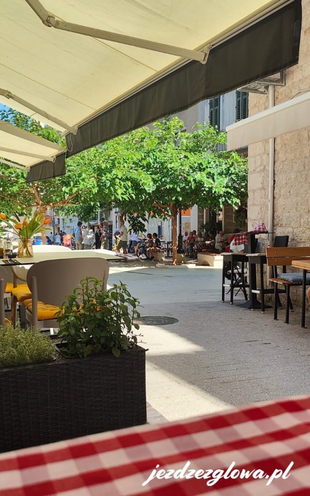 Klimatyczny ogródek restauracyjny w centrum Splitu z kamienną zabudową, zacienionym placem i stolikami dla gości.