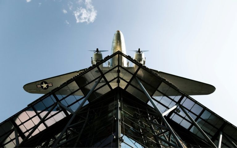 Samolot Rosinenbomber nad wejściem do Deutsches Technikmuseum w Berlinie, widziany od dołu na tle szklanej konstrukcji i błękitnego nieba