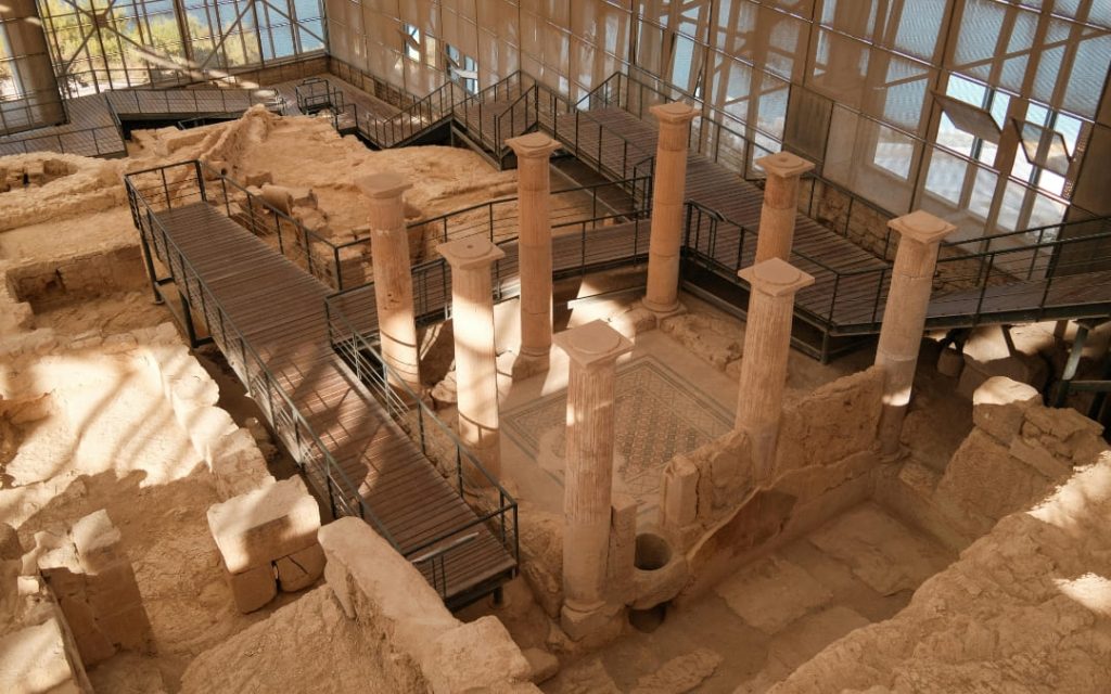 Stanowisko archeologiczne z kamiennymi kolumnami, mozaikową posadzką i pozostałościami starożytnej budowli pod zadaszeniem
