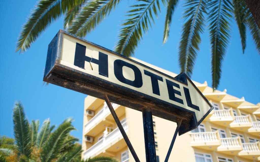 Tablica z napisem hotel, palmy i budynek noclegowy w słonecznym kurorcie 