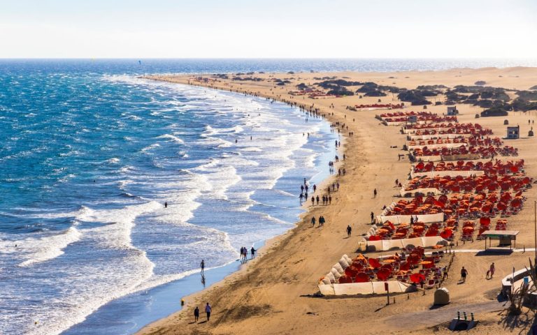 Turyści na Playa del Inglés z wydmami Maspalomas w tle