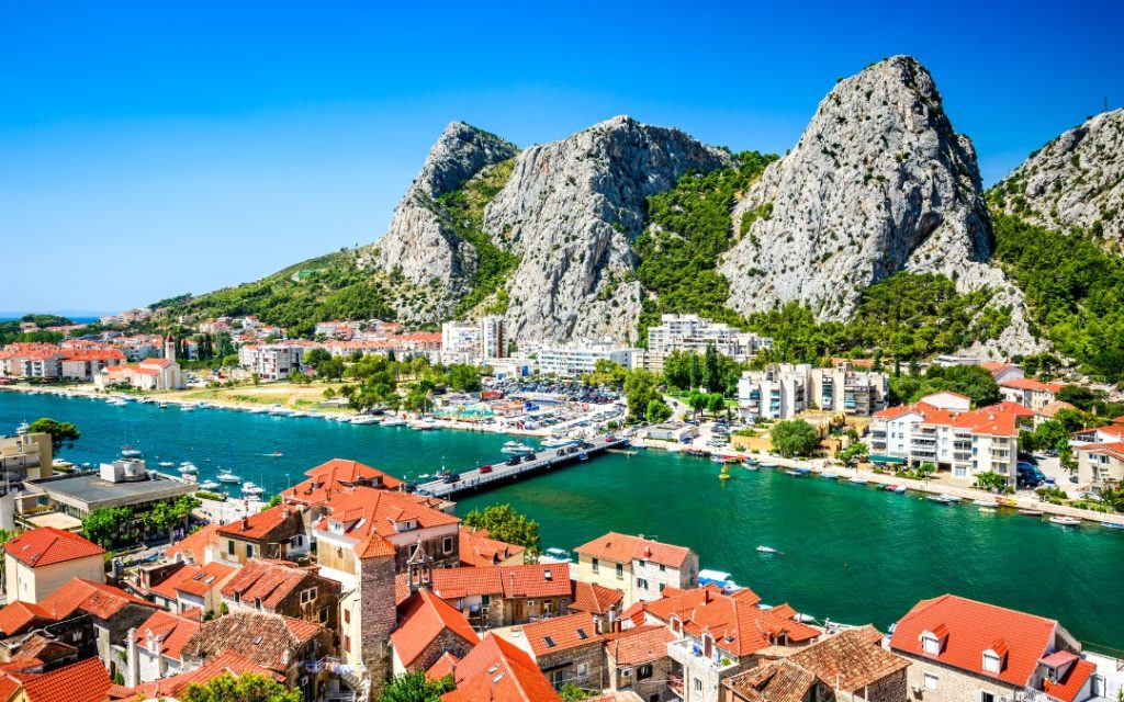 Widok na Omiš z czerwonymi dachami zabudowy, zieloną rzeką Cetiną i wapiennymi szczytami masywu Omiška Dinara w tle