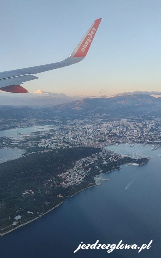 Widok na Split z samolotu podczas lądowania, z wybrzeżem Adriatyku, zabudową miasta i skrzydłem samolotu w kadrze.
