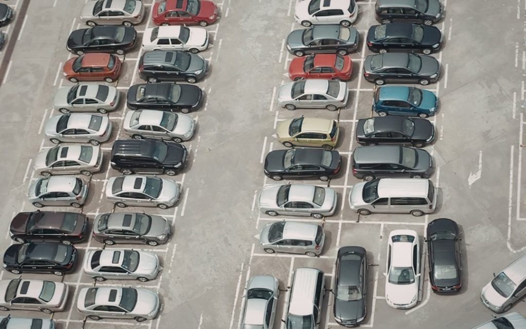 Widok z góry na duży parking z rzędami zaparkowanych samochodów osobowych