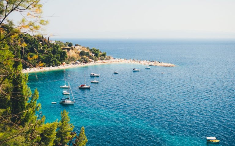 Widok z góry na plażę Kašjuni z turkusową wodą, zacumowanymi łodziami i zalesionym wybrzeżem