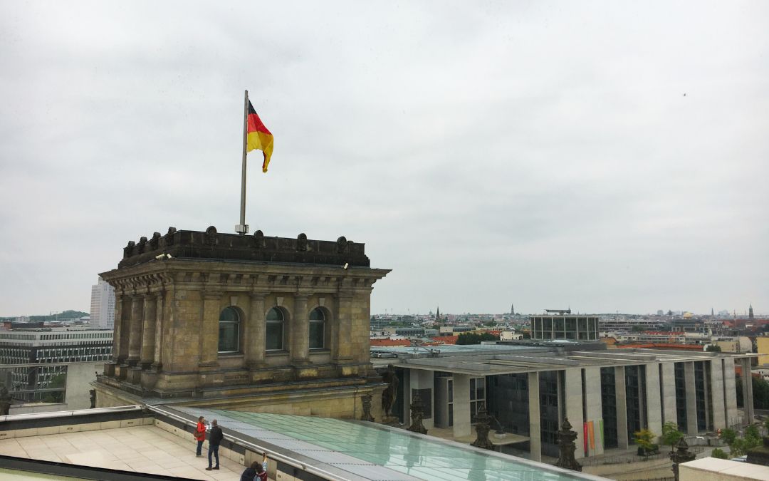 Widok z tarasu Reichstagu w Berlinie na zabytkową część budynku z niemiecką flagą oraz panoramę dzielnicy