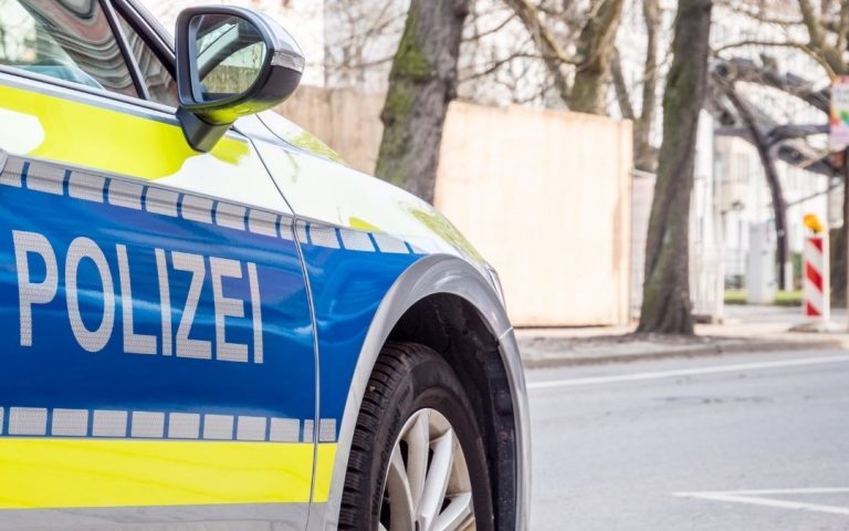Zbliżenie na niemiecki radiowóz policyjny z napisem Polizei na drzwiach, zaparkowany przy miejskiej ulicy