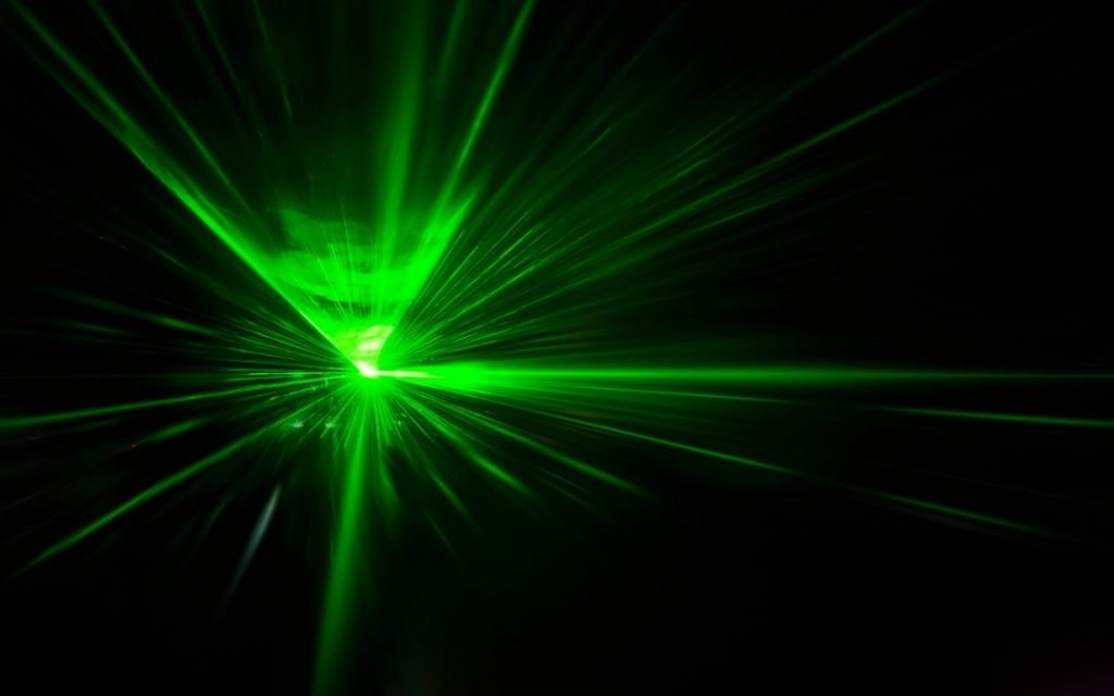 Zielone promienie lasera rozchodzące się w ciemności, tworzące dynamiczny efekt świetlny na czarnym tle