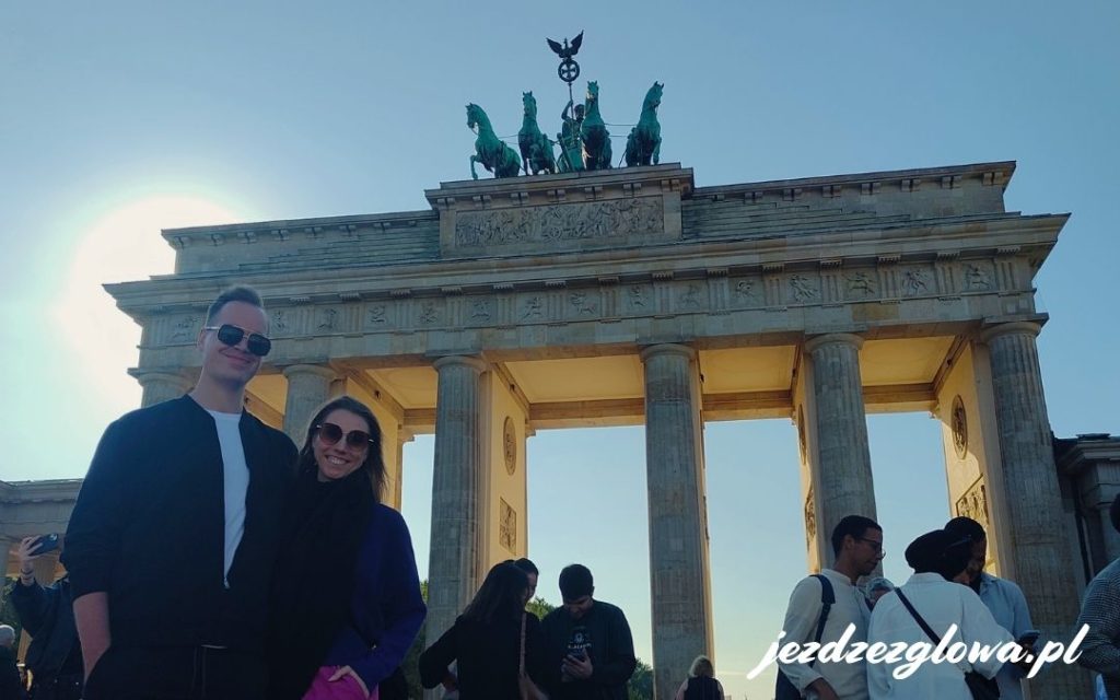 osoby pozujące przed Bramą Brandenburską w Berlinie, z Kwadrygą na szczycie i turystami wokół zabytkowego monumentu