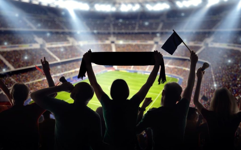 Grupa kibiców dopingująca drużynę na pełnym stadionie piłkarskim przy świetle reflektorów