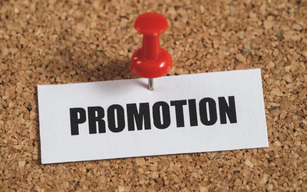 Kartka z napisem promocja przypięta pinezką do tablicy 